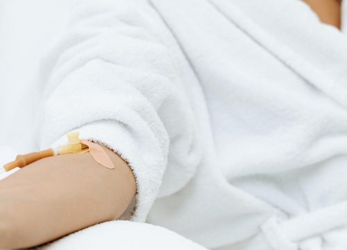 Photo of a woman getting IV therapy and holding a class of cucumber water